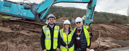 3 people in hi viz standing in front of a digger