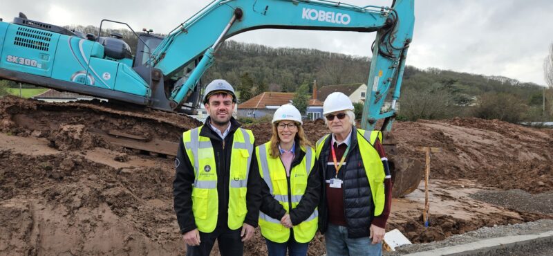3 people in hi viz standing in front of a digger