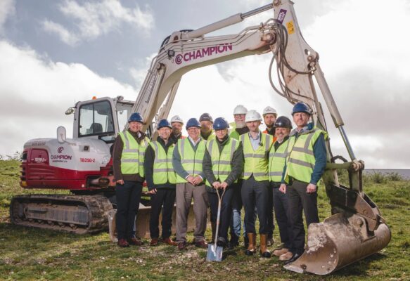 People in hi viz and hard hats under the arm of a digger
