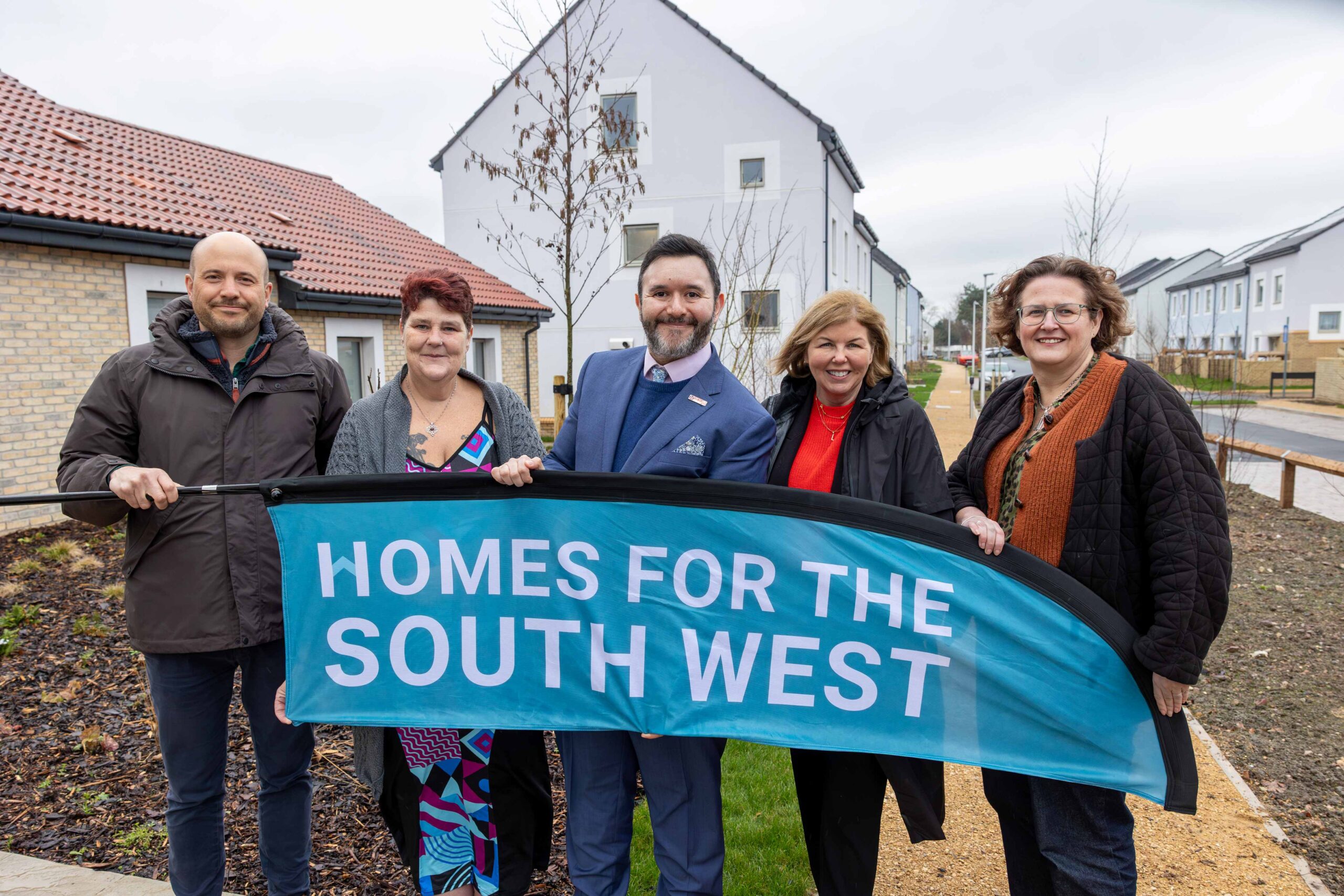 Five people standing in front of new homes holding a flag that says homes for the south west.  
