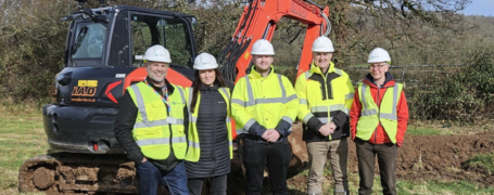 5 people standing a field in front of a digger
