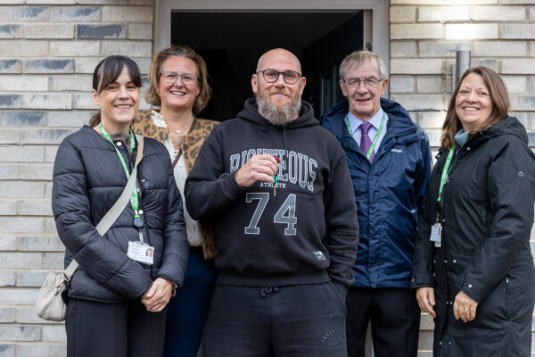 5 People in front of a house with a man holding keys in the centre