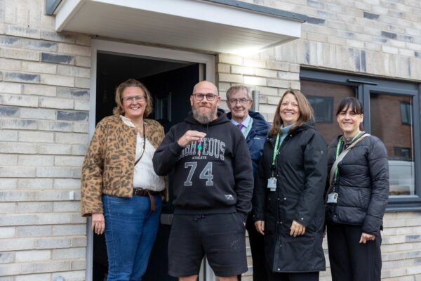 5 people standing outside a house, person second from left proudly hold keys